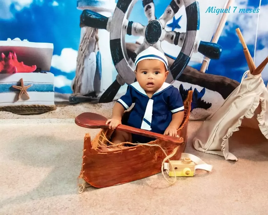 Bebê de 7 meses de roupa de marinheiro remando em barquinho de madeira.