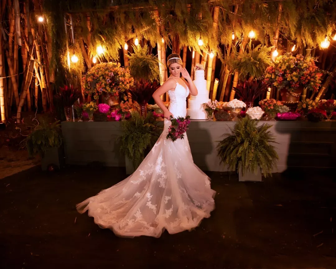Noiva de vestido longo em jardim iluminado à noite.
