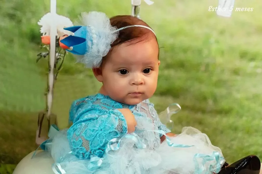 Bebê de 5 meses com tiara azul em cenário de jardim.