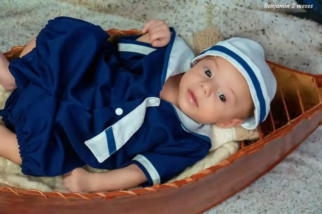 Bebê de 2 meses de roupa de marinheiro deitado em barquinho de madeira.