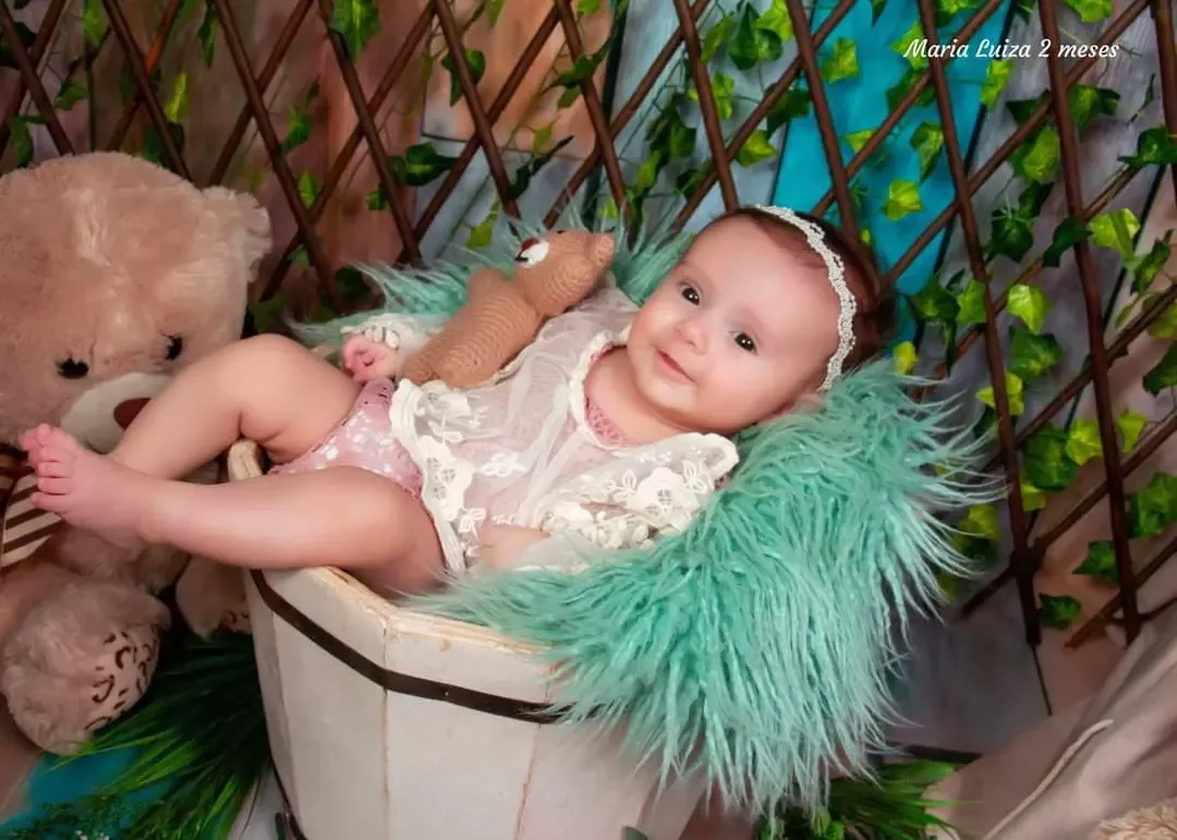 Bebê de 2 meses de vestido de renda em cesto com manta verde.