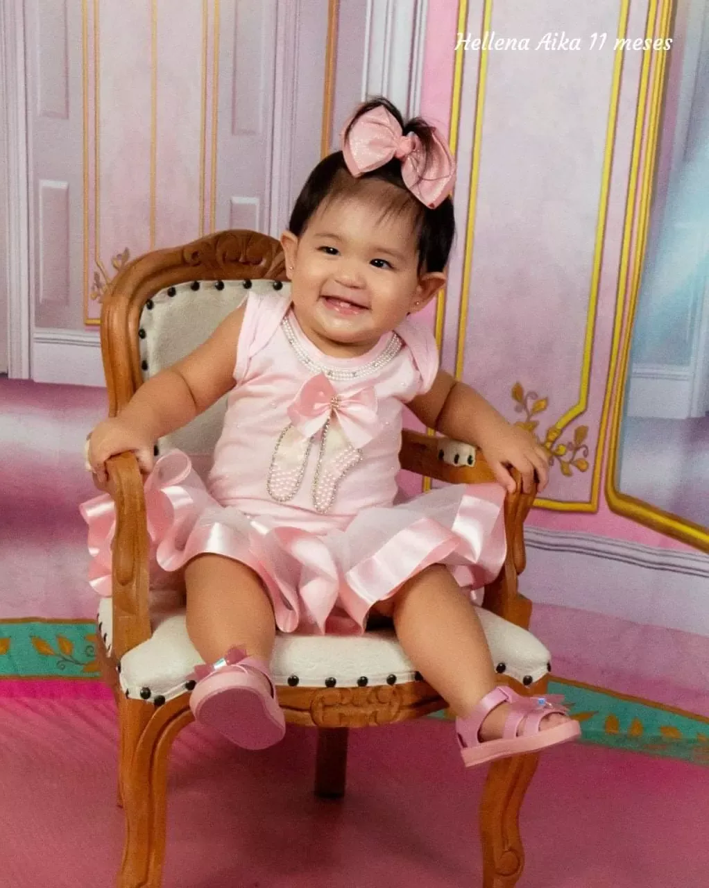 Bebê de 11 meses de vestido rosa sentada em poltrona dourada.