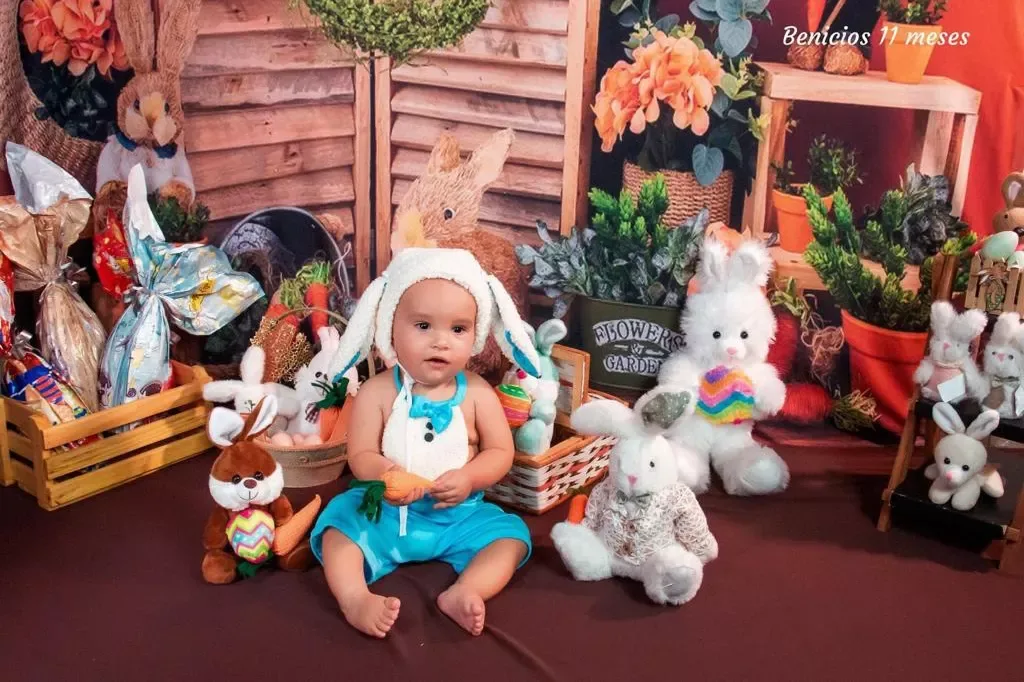 Bebê de 11 meses com touca de coelho em cenário de Páscoa.