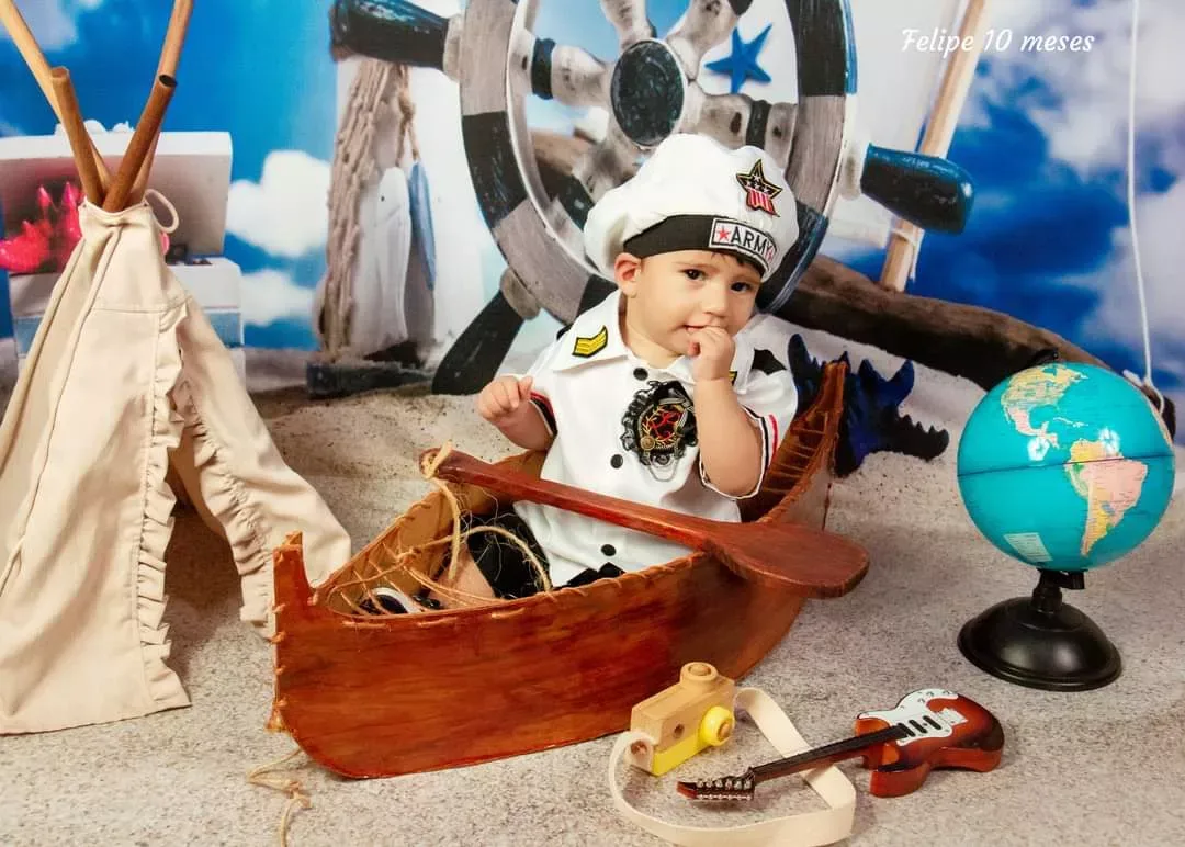 Bebê de 10 meses de roupa de marinheiro em barquinho com globo terrestre.
