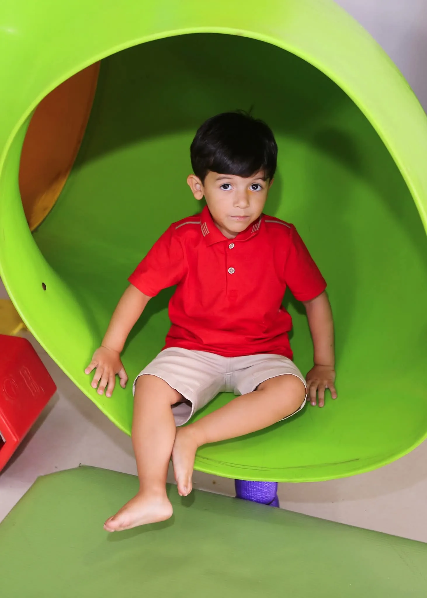 Menino de camisa vermelha sentado em brinquedo verde.