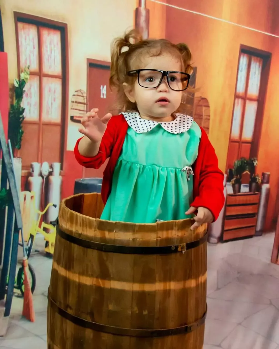 Menina de óculos e vestido verde dentro de um barril de madeira.
