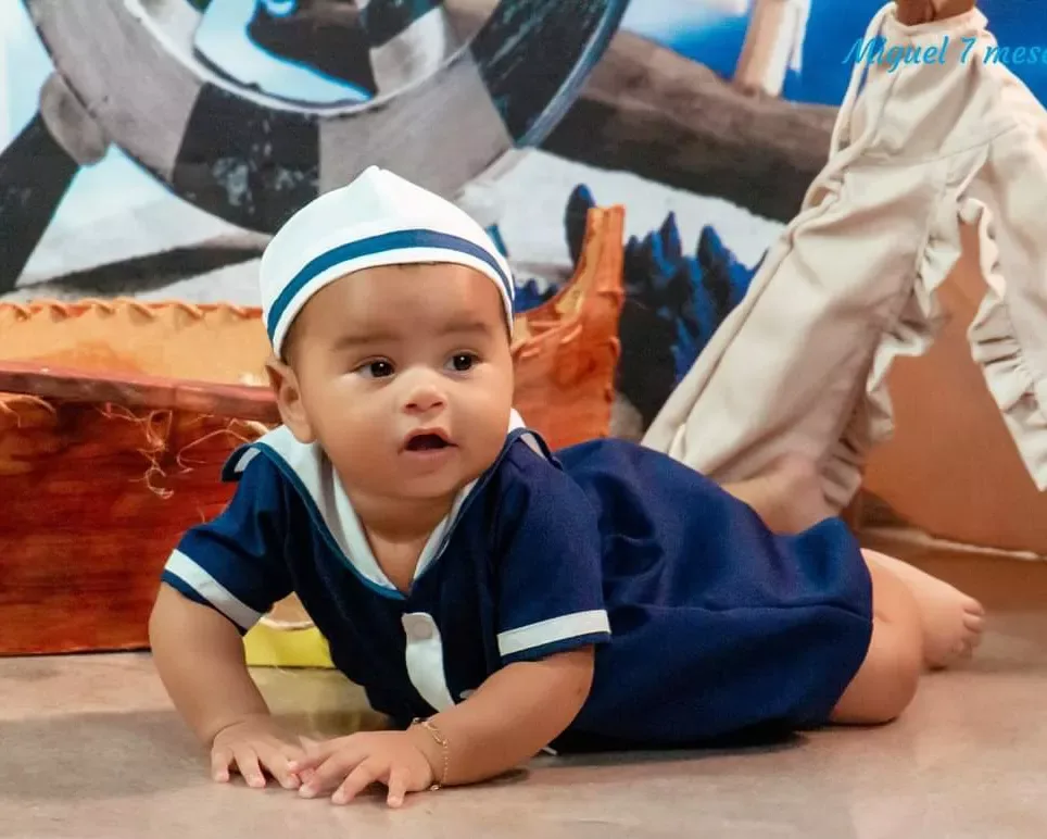 Bebê de 7 meses de roupa de marinheiro engatinhando em cenário de praia.