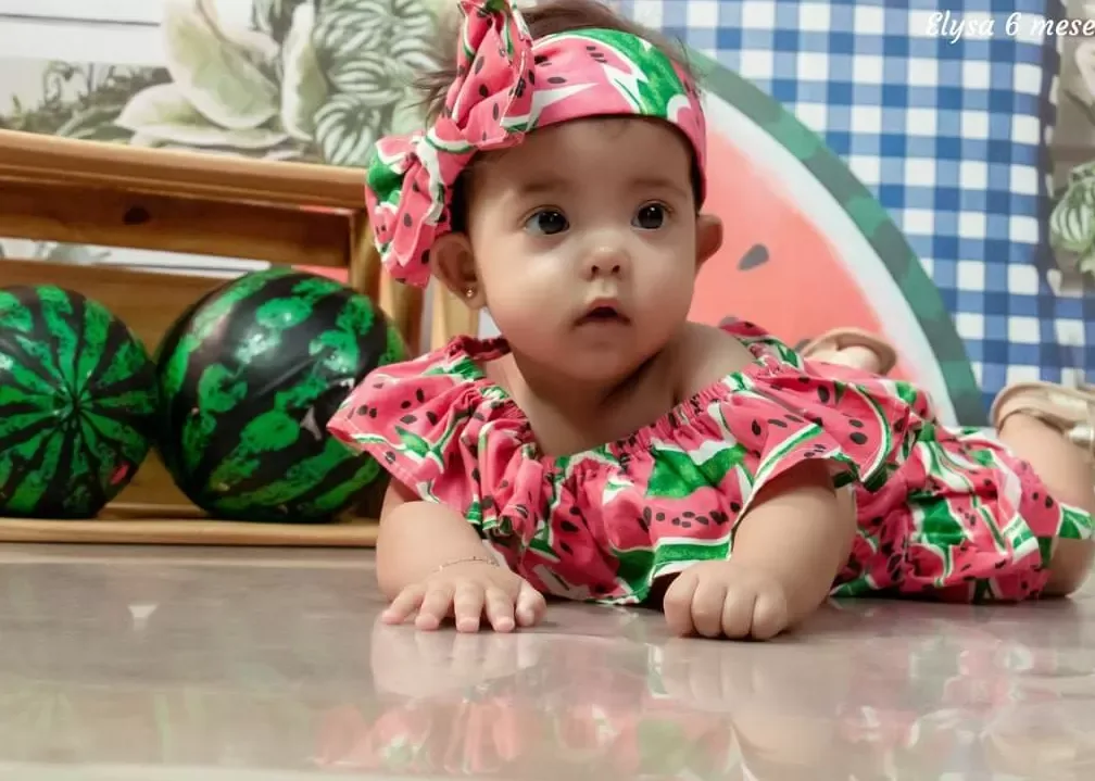 Bebê de 6 meses deitada de bruços em cenário de piquenique com melancias.