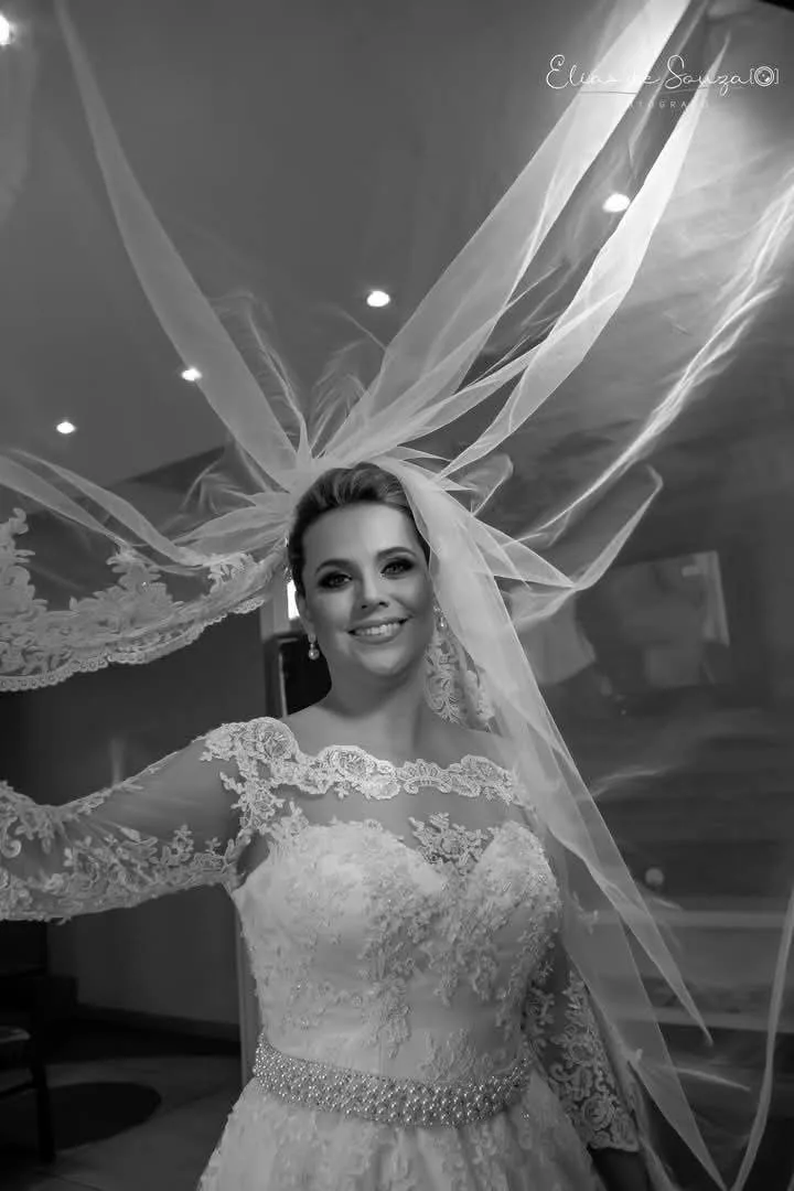Noiva sorrindo sob o véu, em preto e branco.