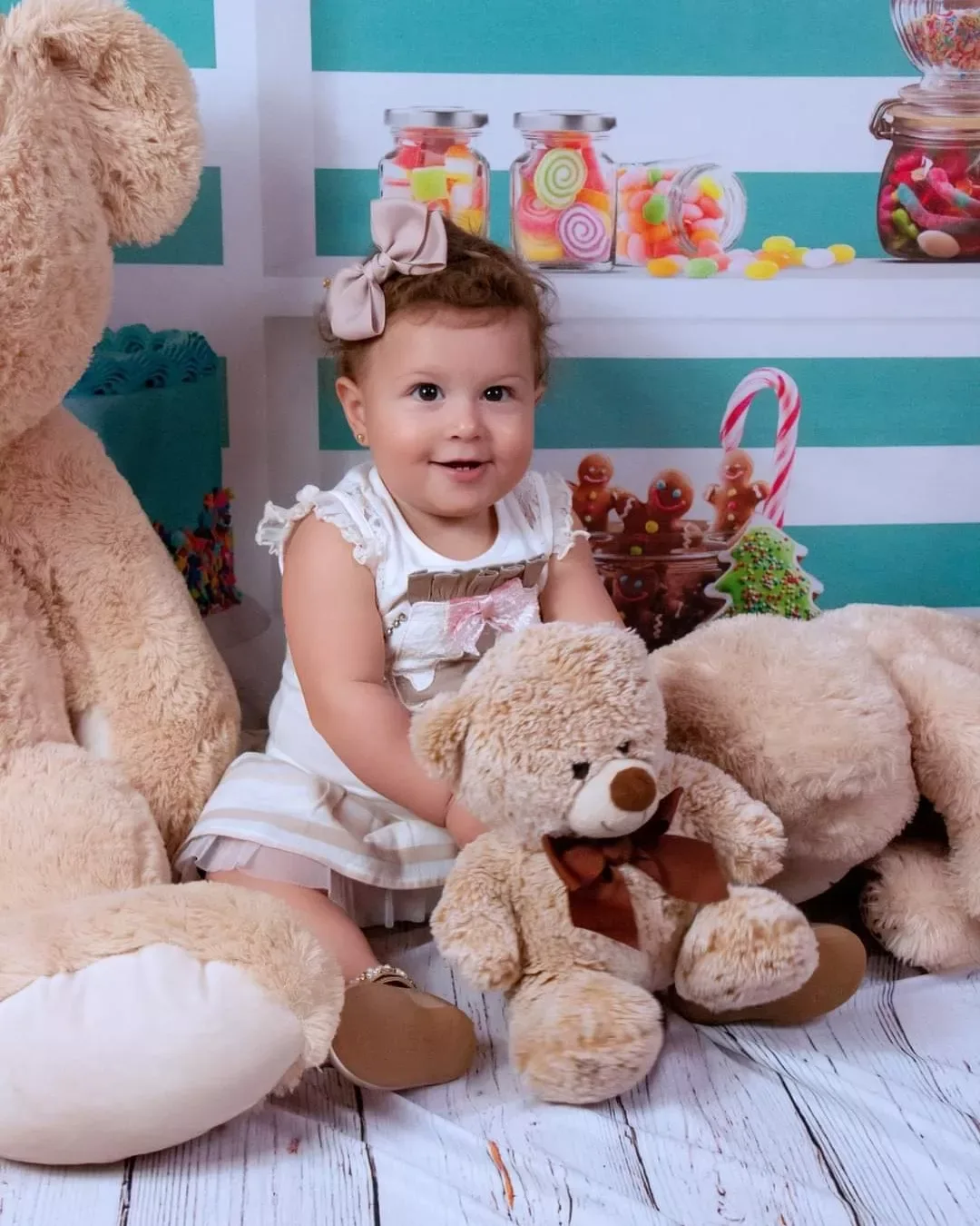 Menina de 1 ano sentada entre ursos de pelúcia e potes de doces.