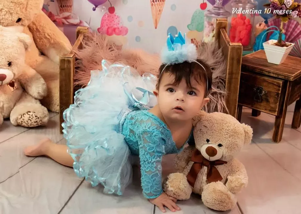 Bebê de 10 meses de saia de tule azul engatinhando entre ursos de pelúcia.
