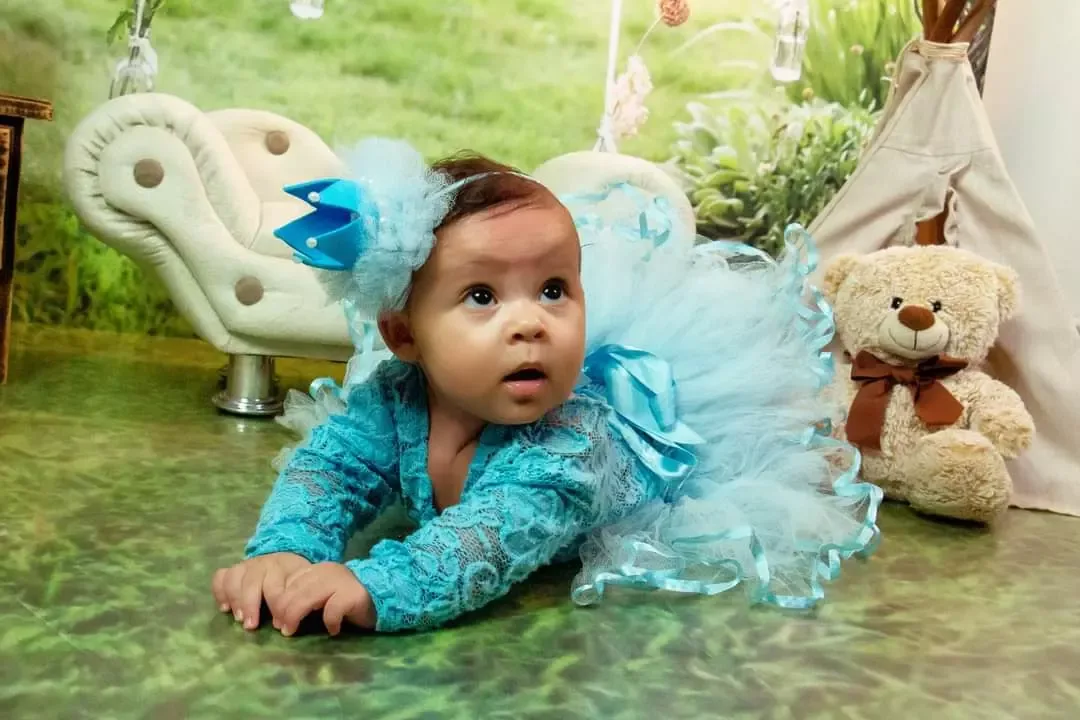 Bebê de 5 meses de tule azul deitada de bruços em cenário de jardim.