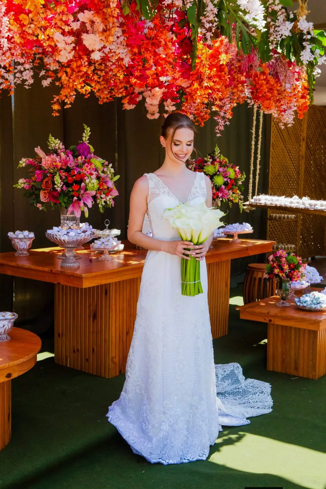 Noiva com buquê de flores brancas diante de arranjo de flores vermelhas.