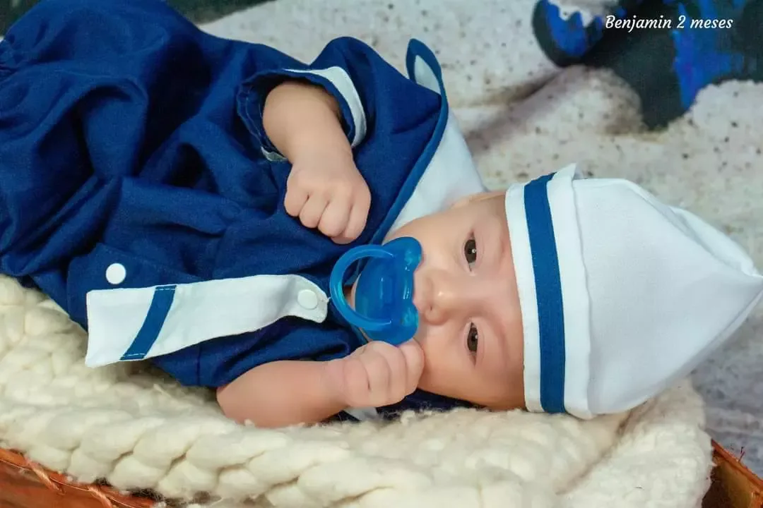 Bebê de 2 meses de roupa de marinheiro com chupeta, deitado em manta clara.