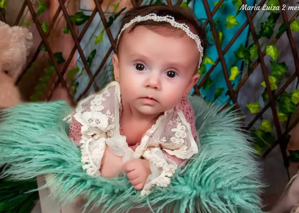 Bebê de 2 meses com faixa de pérolas deitada sobre manta verde.