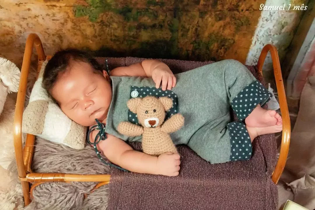 Recém-nascido de 1 mês dormindo em cama de madeira com urso de pelúcia.
