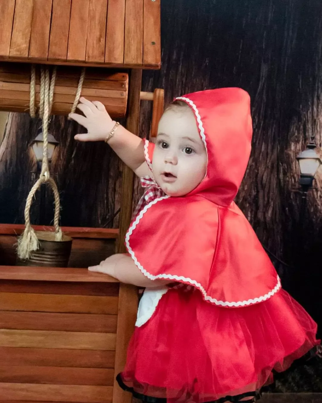 Bebê de capa vermelha apoiada em um poço de madeira.