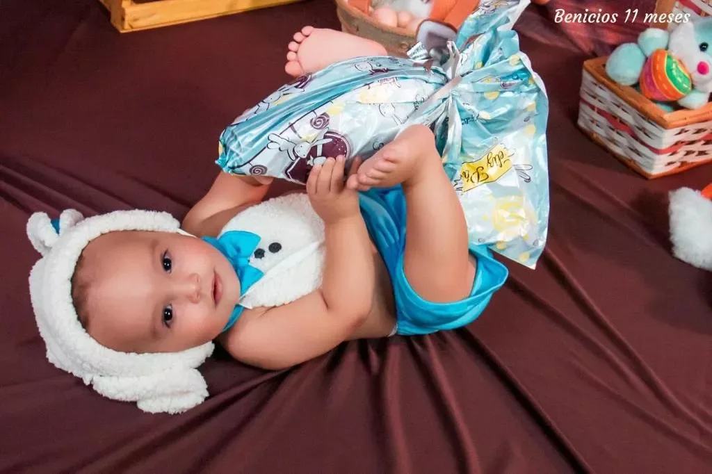 Bebê de 11 meses com touca de coelho deitado sobre manta marrom.