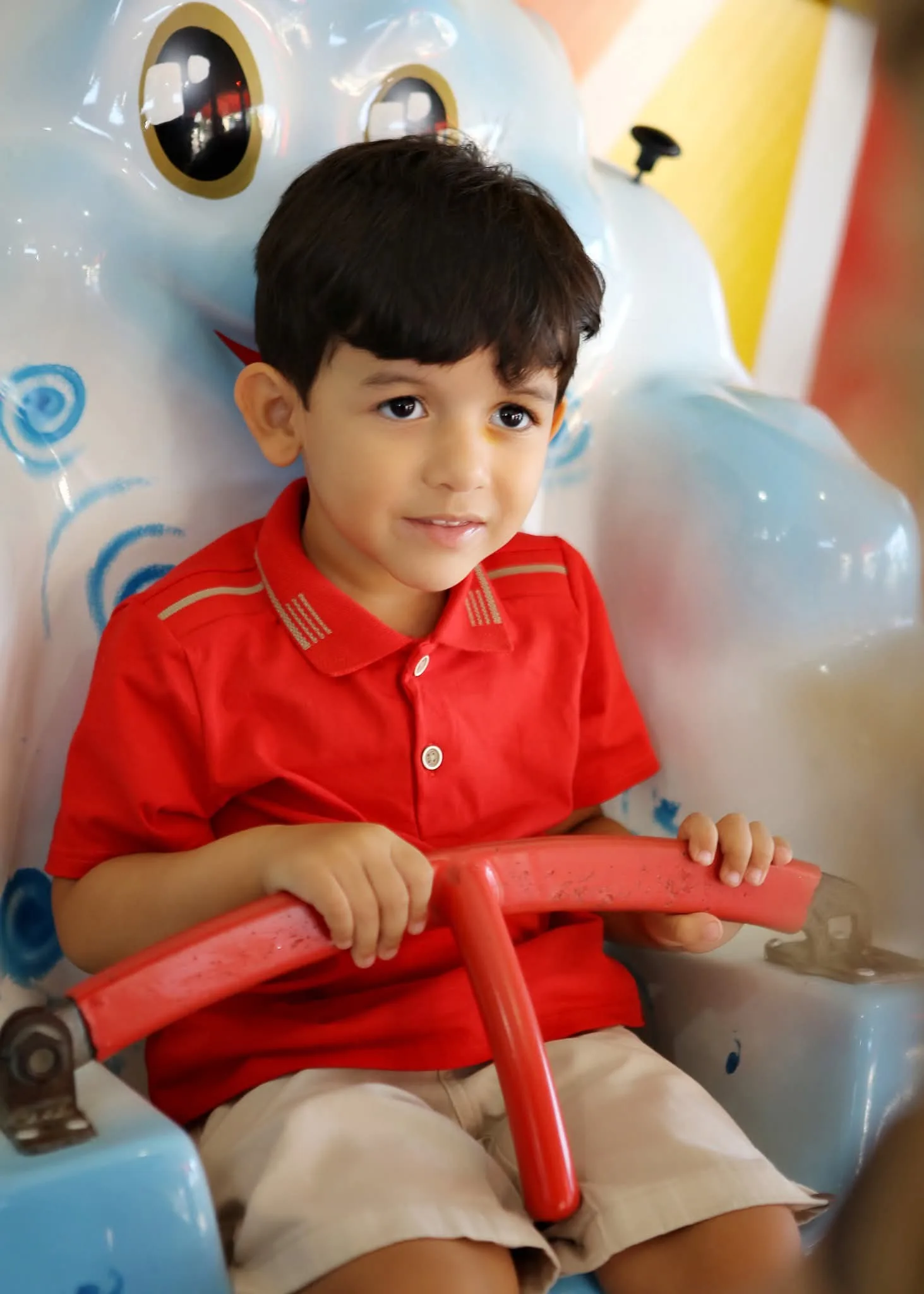Menino de camisa vermelha sentado em brinquedo de parque.