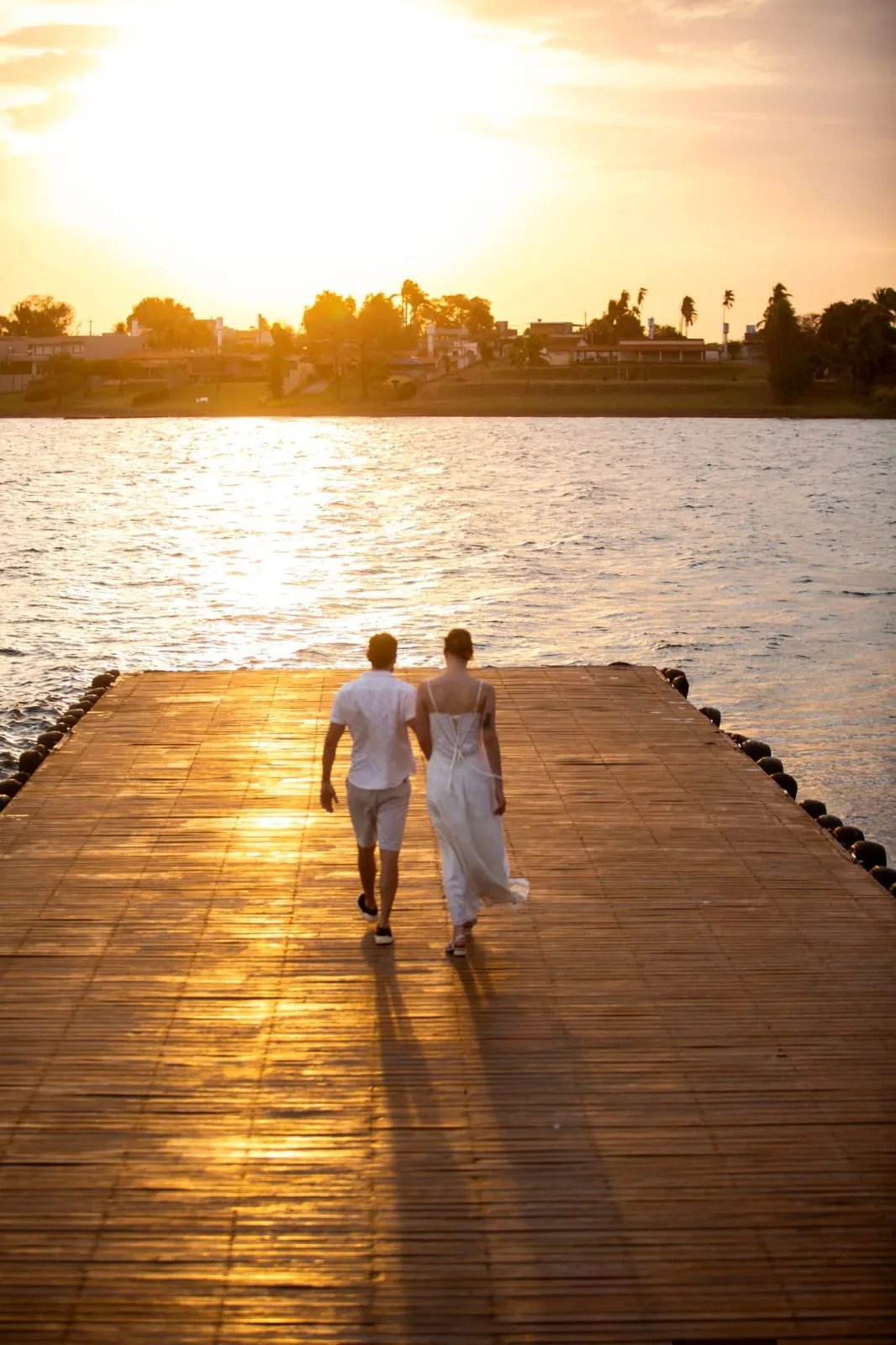 Casal caminhando em píer ao pôr do sol.