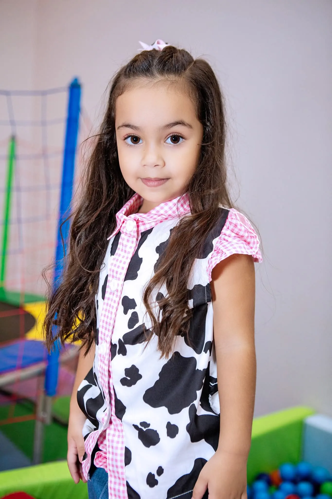 Menina de roupa estampada de vaca em pé, em espaço de brincar.