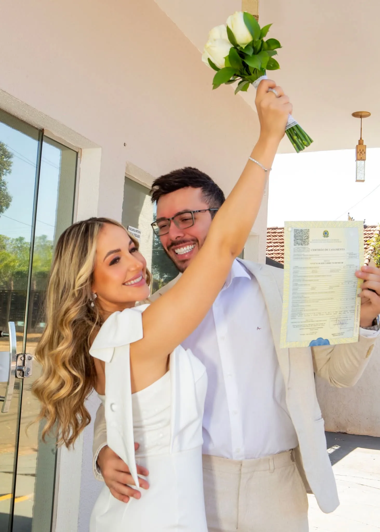 Casal comemorando com buquê e certidão de casamento.