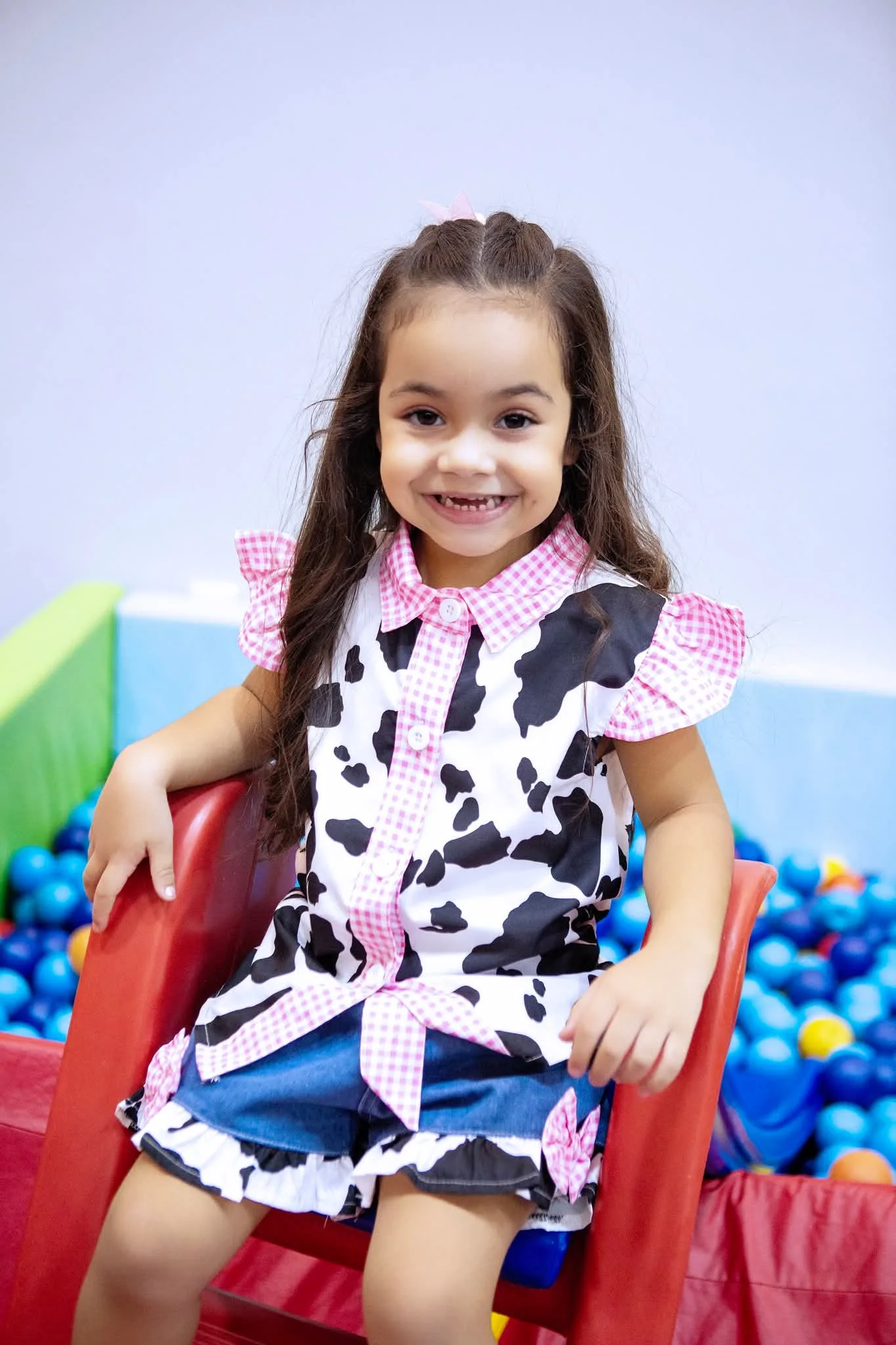 Menina de roupa estampada de vaca sentada em escorregador vermelho.